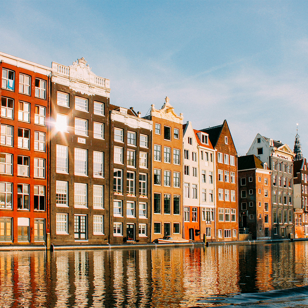 Historic Amsterdam buildings along a tranquil canal, under a clear blue sky.