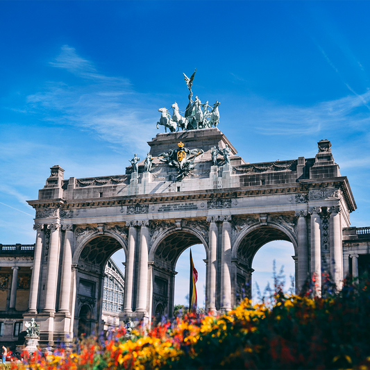Triumphal arch with intricate sculptures and statues on top against a clear blue sky. Vibrant flowers in foreground.