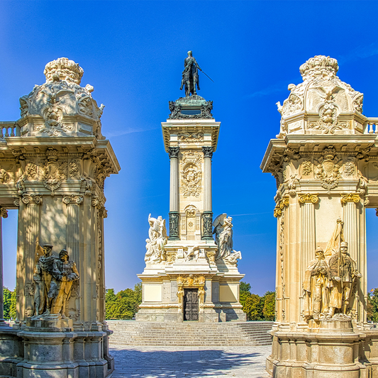 Decorative stone archway with statues and a central monument against a clear blue sky.