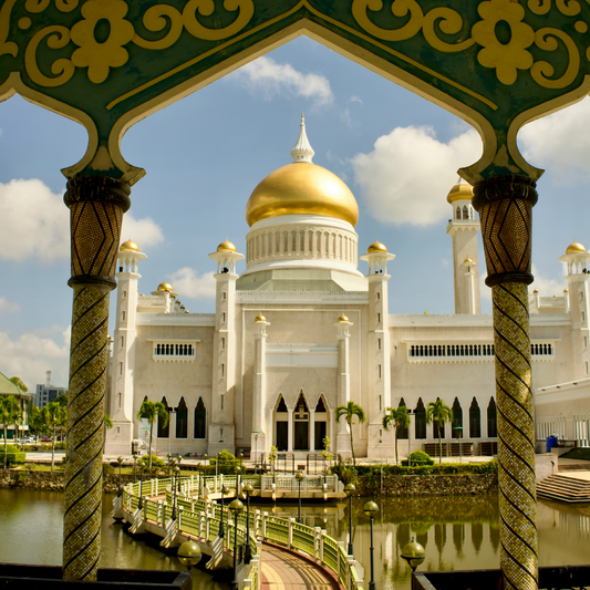 The Omar Ali Saifuddien Mosque in Brunei, framed by ornate green and gold archways, with its iconic golden dome and white minarets reflecting under a blue sky.