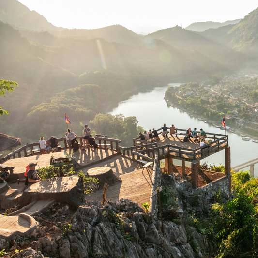 A hilltop wooden viewing platform overlooks a sweeping bend in the Nam Ou River winding through misty mountains and a valley village in northern Laos.